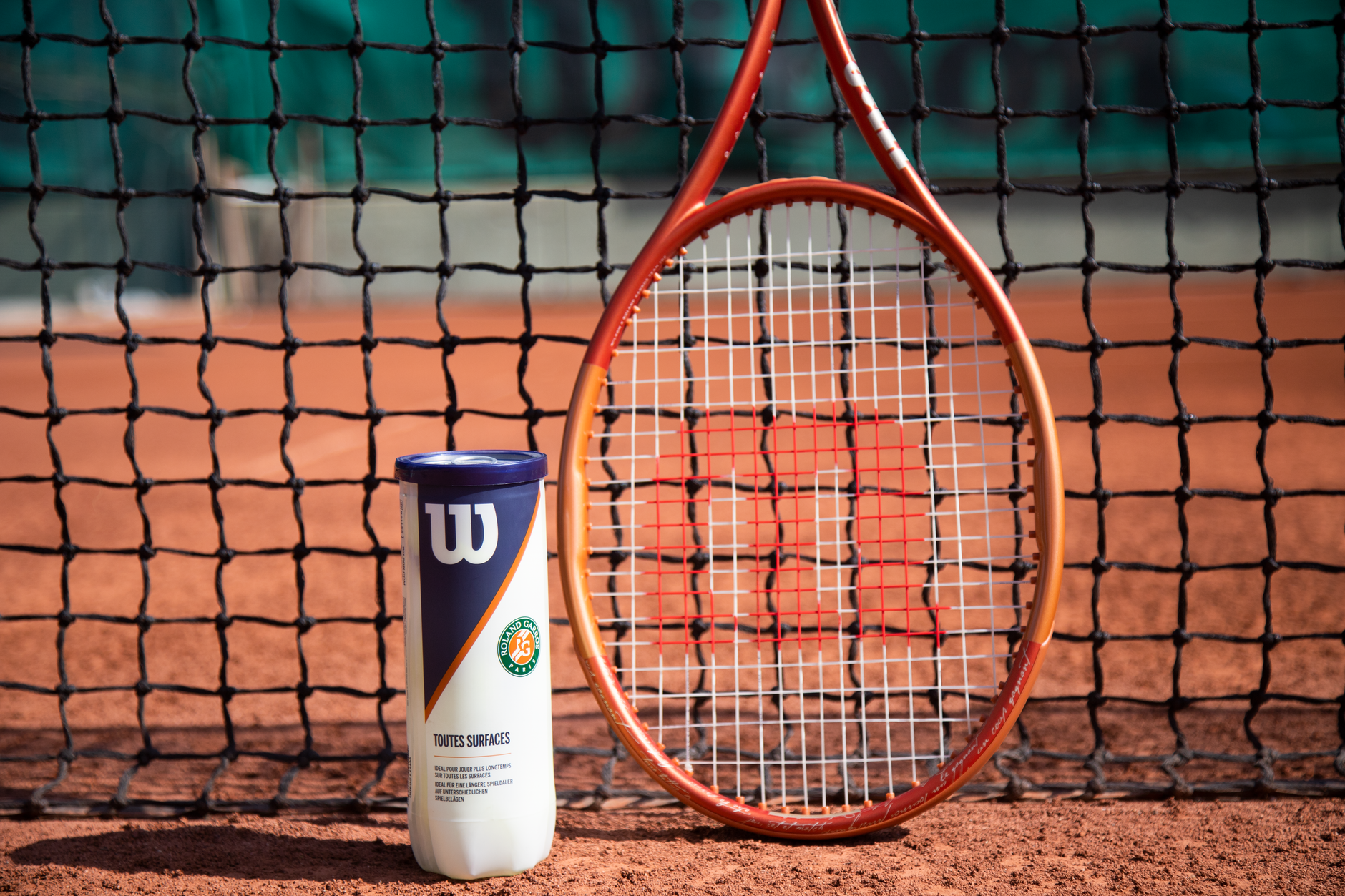 Tennis racquet and a can of balls in front of a net on a clay court