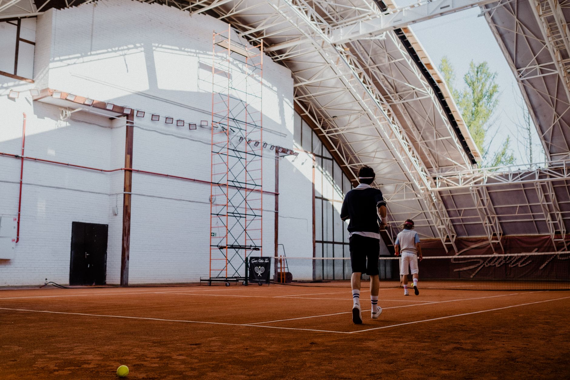 Two players on an indoor clay tennis court with natural lighting