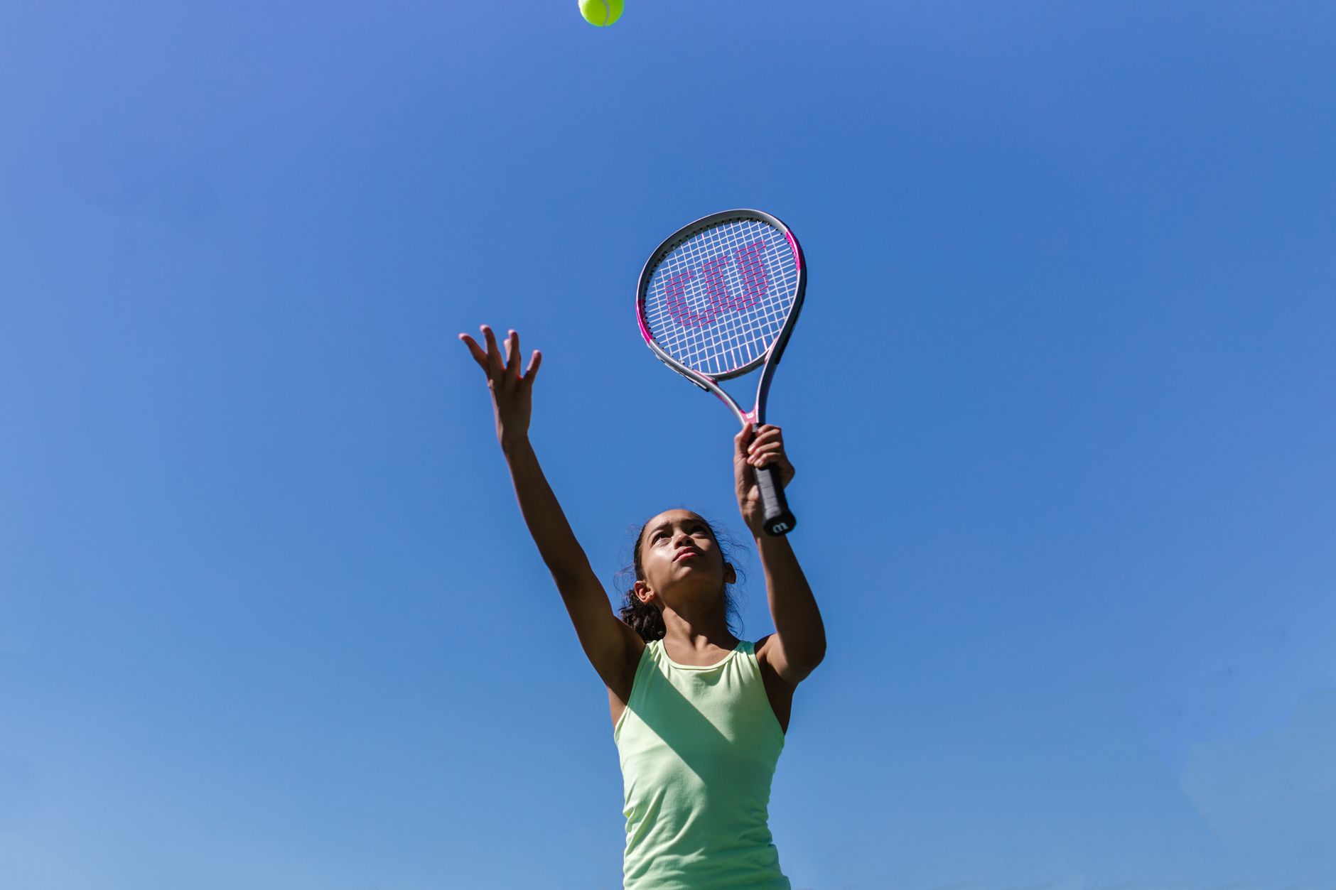 Player practicing a tennis serve outdoors on a sunny public court