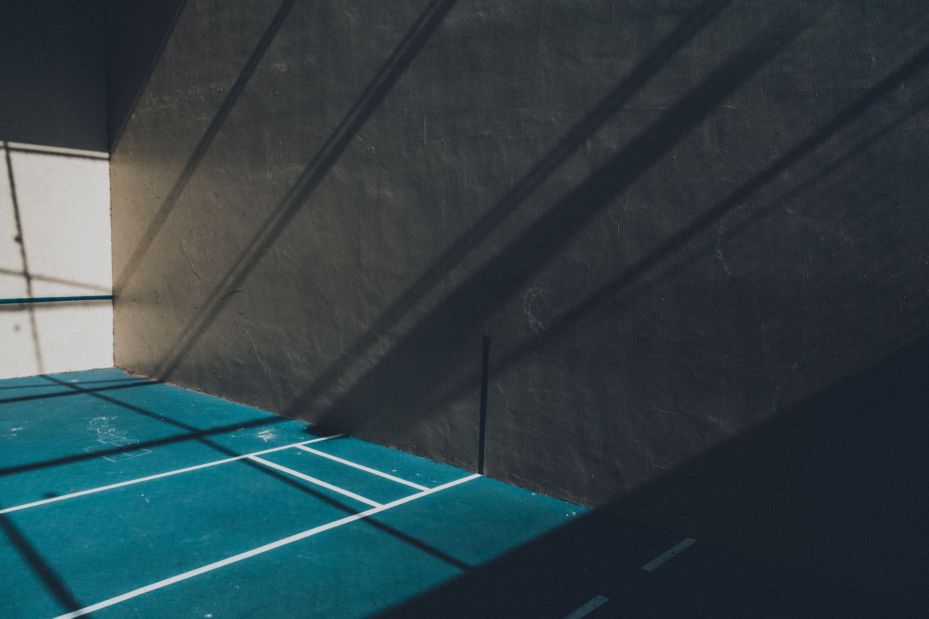Empty indoor squash court with dramatic shadows and blue flooring