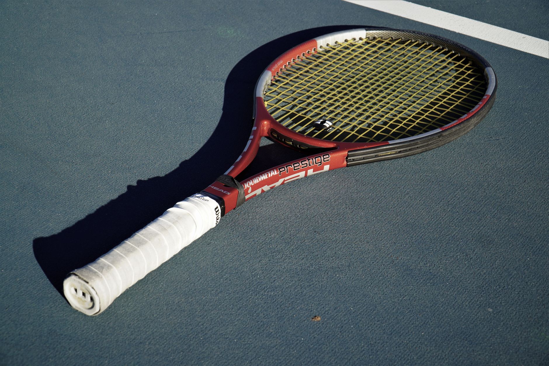 Tennis racket resting on a sunlit blue court