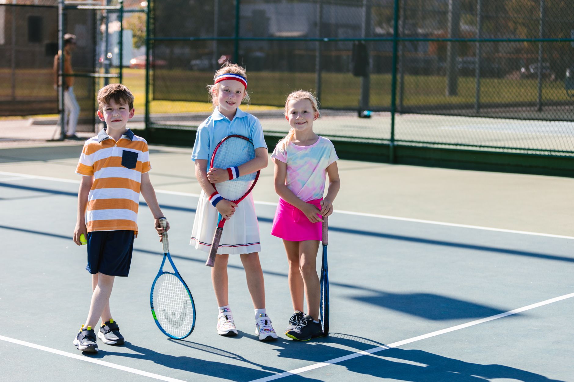 A group of kids smiling and playing tennis together outdoors on a sunny day