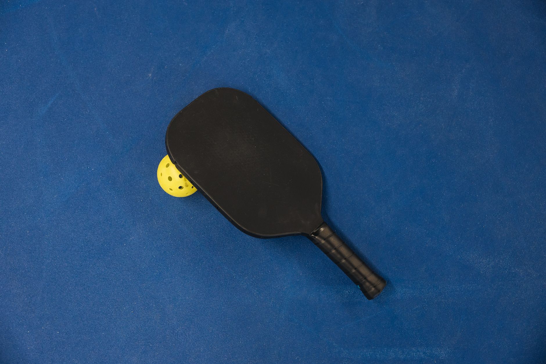 Pickleball paddle and ball resting on a court surface