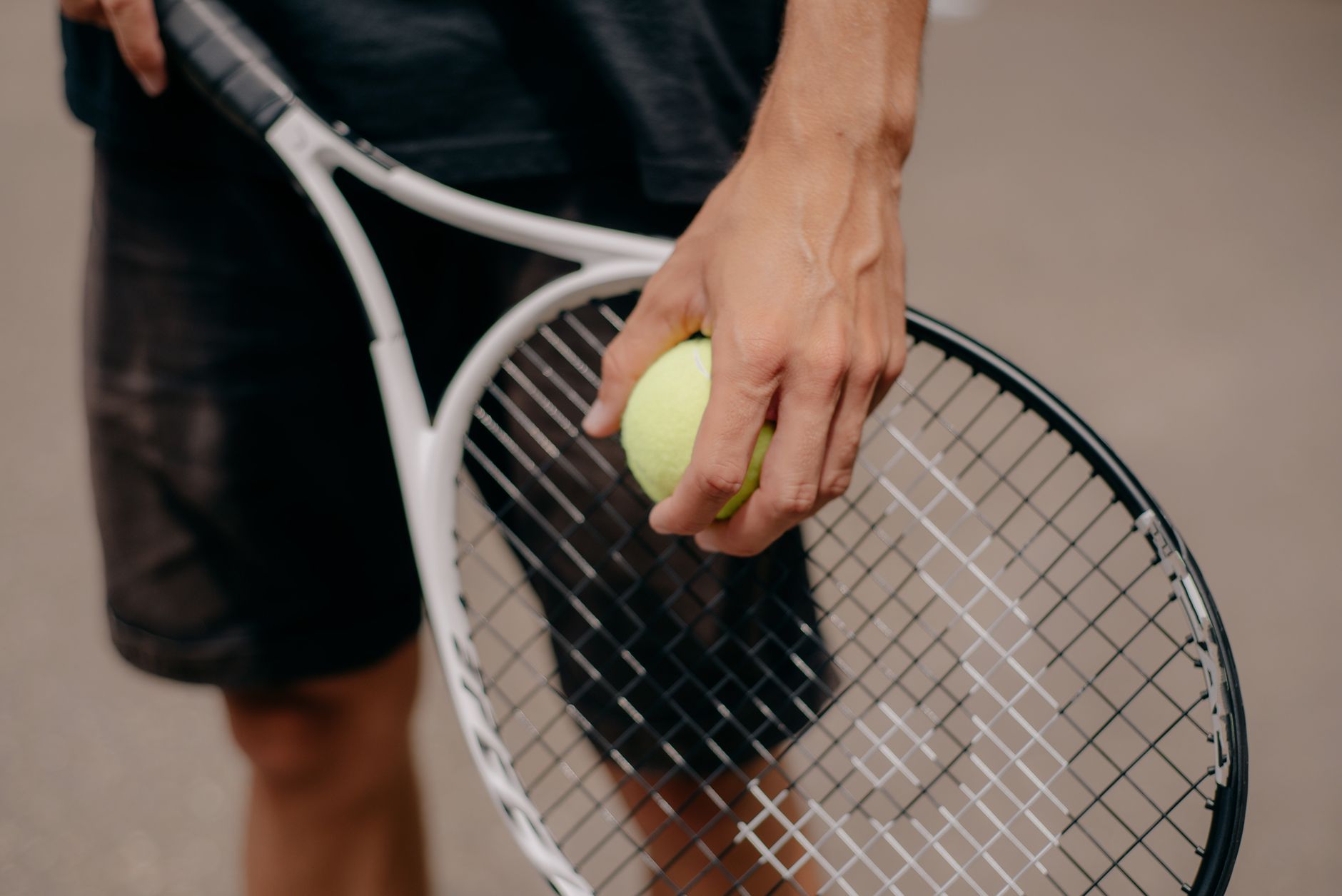 Close-up of a tennis player holding a ball and racket before serving