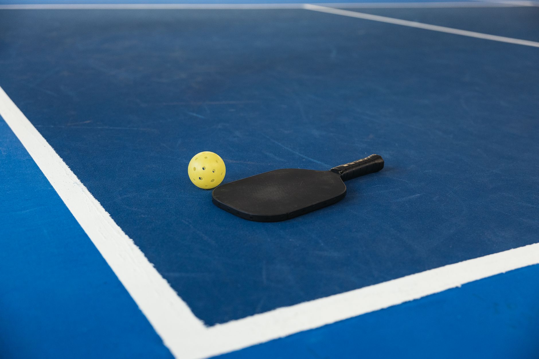 Pickleball paddle and yellow ball resting on a blue court
