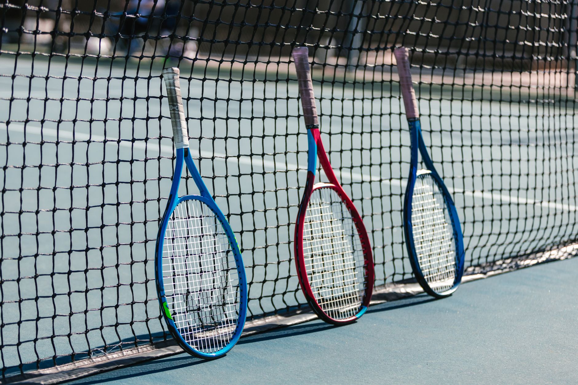 Three tennis rackets leaning against a net on an outdoor court